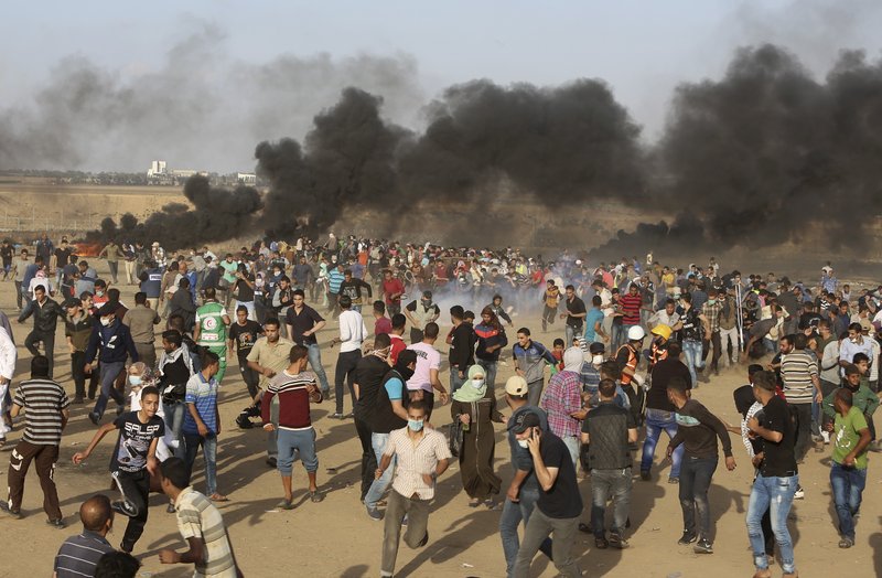 Palestinian protesters run for cover from teargas fired by Israeli troops during a protest at the Gaza Strip's border with Israel, Friday, May 11, 2018. Gaza activists burned tires near the sealed border with Israel on Friday in a seventh weekly protest aimed at shaking off a decade-old blockade of their territory. Israeli soldiers fired tear gas volleys from the other side of the border fence. (AP Photo/Adel Hana)