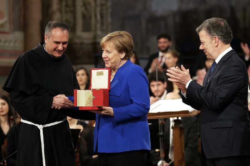 The Rev. Mauro Gambetti presents the St. Francis Lamp peace prize to German Chancellor Angela Merkel on Saturday in St. Francis’ Basilica in Assisi, Italy. At right is Colombian President Juan Manuel Santos, winner of the 2016 Nobel Peace Prize, who introduced Merkel.  