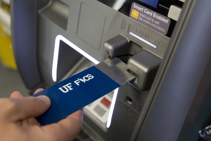 In this April 18, 2018, photo, a detective with the New York City Police Department uses a detection device that indicates if a credit card skimmer is in use at an ATM machine at a New York convenience store. The device is under development by the Florida Institute for Cybersecurity Research. (AP Photo/Mark Lennihan)