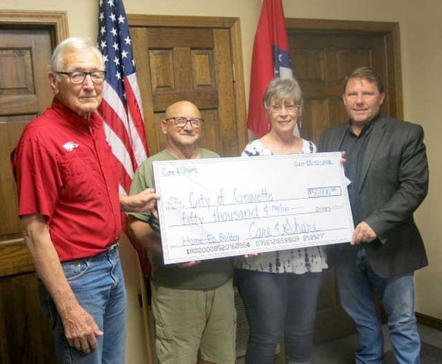 Westside Eagle Obsever/SUSAN HOLLAND John Mitchael (left), Gravette Historical Museum commission member, accepts a check for $50,000 from Bo Roberts and Wilma Fladager, representatives of Care and Share, at the May committee of the whole meeting. Mayor Kurt Maddox represents the city of Gravette in accepting the Care and Share donation, which is to be used for the museum commission's renovation of the old home economics building.