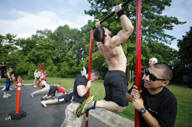 FILE PHOTO/DAVID GOTTSCHALK U.S. Marine Corps Staff Sgt. Victor Fernandez (right) braces a pull-up bar for cross-fit athletes to perform butterfly pull-ups during a past Arkansas Support Network Moving Together event. This year's event is set for Saturday at Veterans Memorial Park at Lake Fayetteville.