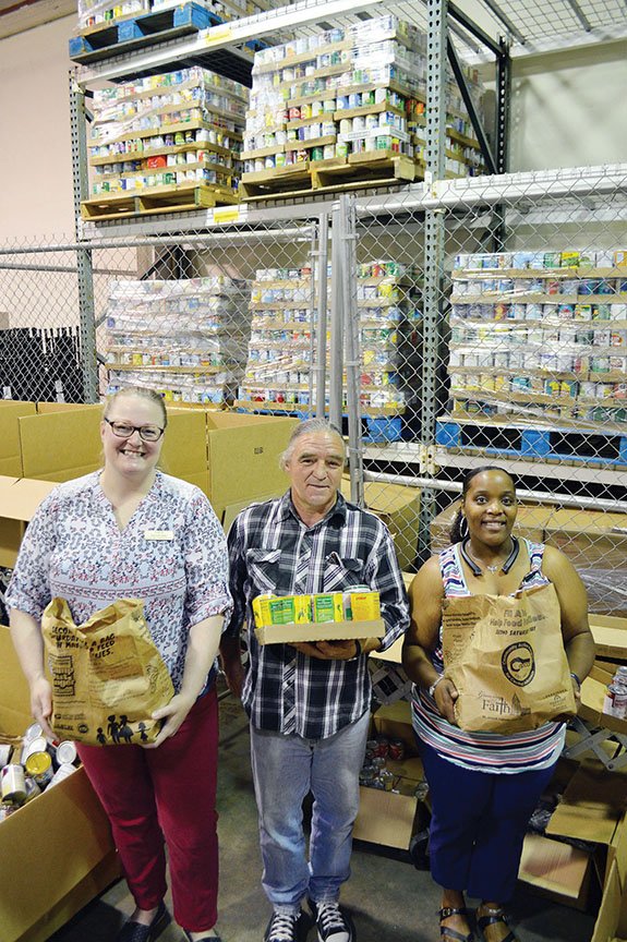 Melissa Allen, from left, community-programs director for the Community Action Program for Central Arkansas in Conway; Walter Callahan, volunteer; and Myracle White, pantry coordinator, hold some of the record 31,340 pounds of food collected by Conway, Mayflower and Vilonia residents through the 26th annual Letter Carriers’ Stamp Out Hunger Food Drive.