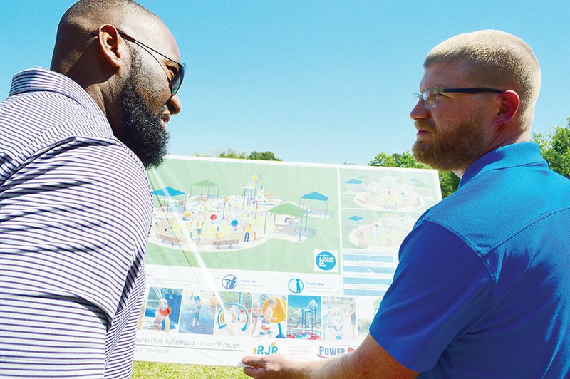 Leo Cummings III, left, director of member engagement for the Conway Area Chamber of Commerce, and Derek Cox, assistant director of Conway Parks and Recreation, look at the plans for the city’s first splash pad during a groundbreaking for the project May 11 in Laurel Park. The 5,485-square-foot splash pad is scheduled to be open July 4, Mayor Bart Castleberry said.