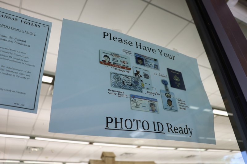 In this May 7, 2018, photo, a sign is posted above the check-in station for an early voting precinct at the Roosevelt Thompson Library in Little Rock warning voters that they will be asked to show an identification card. (AP Photo/Kelly P. Kissel)