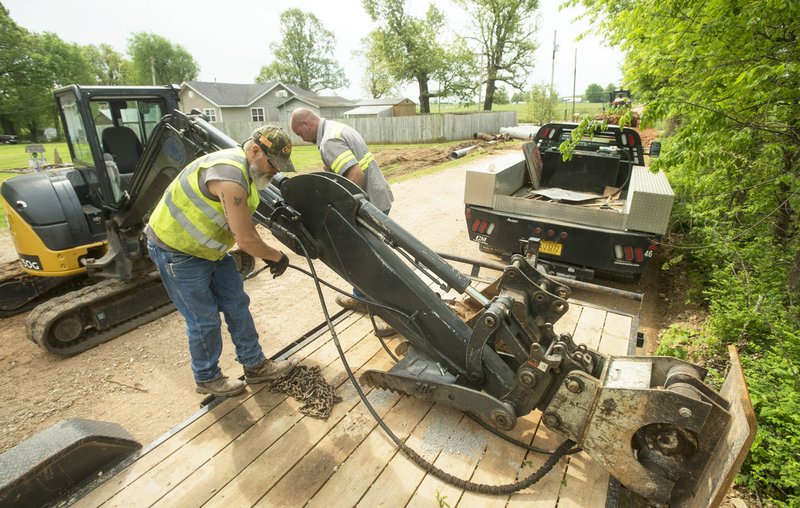 Jack Hutcheson (left) and Shawn Alley with the Benton County Road Department swap a bucket for a compactor attachment on an excavator May 10 while replacing drainage culverts and grading the road surface along Accident Road near Springdale. 
