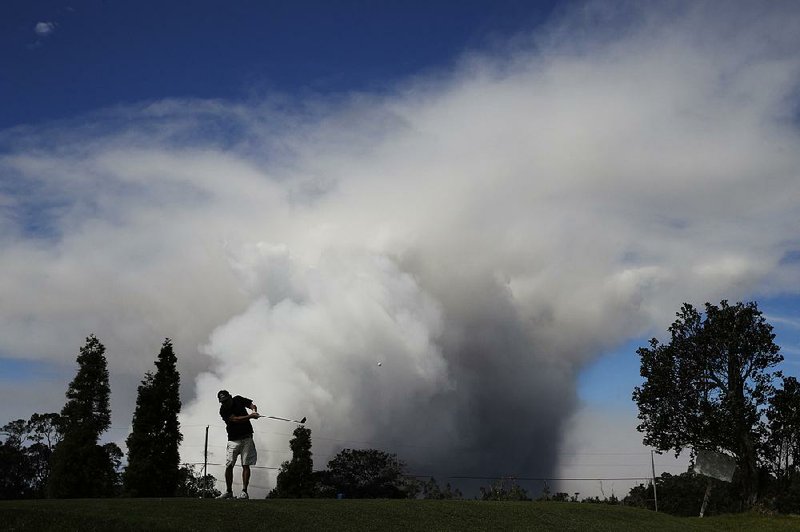 Mike Walls plays golf in Volcano, Hawaii, on Monday as a plume of ash rises from the summit of Kilauea volcano. Tourism officials insist that most of the island is safe for visitors. 

