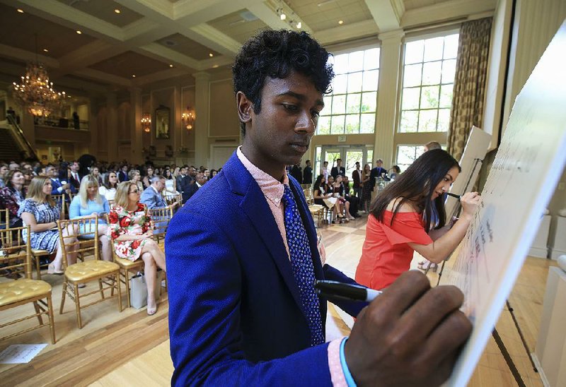 Little Rock Central High School students Anil Chakka (left) and Julianne Chung sign their names Monday during an event to celebrate college-bound Little Rock School District seniors at the Governor’s Mansion. Chakka plans to attend Vanderbilt University and Chung plans to attend Rhodes College. 
