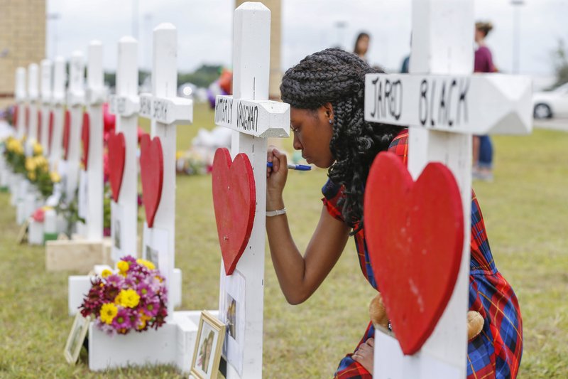 Santa Fe High School freshman, Jai Gillard writes messages on each of the 10 crosses in front the school Monday, May 21, 2018, in Santa Fe. Gillard, was in the art class Friday morning, knew all of the victims of the shooting. Texas Governor Greg Abbott has called for a moment of silence at 10 a.m. and came to the school to participate. (Steve Gonzales/Houston Chronicle via AP)

