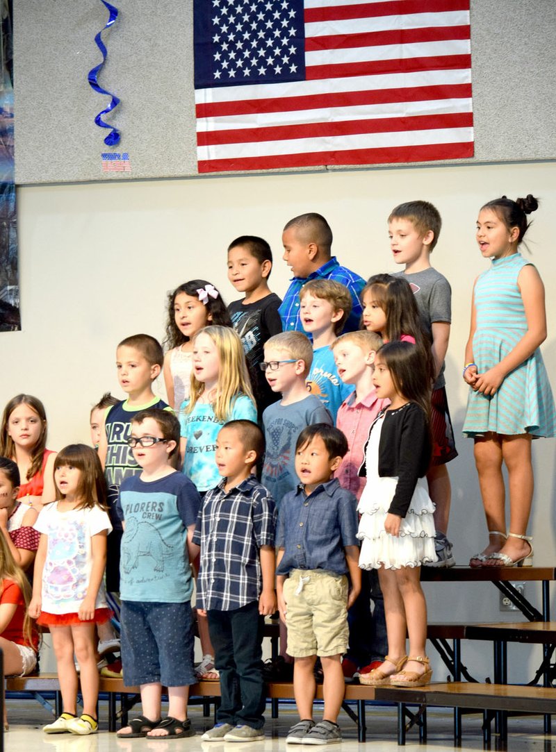 Westside Eagle Observer/MIKE ECKELS With the flag as a backdrop, first graders from Northside Elementary perform a medley of patriotic tunes during USA Night at the school's cafeteria in Decatur May 10.