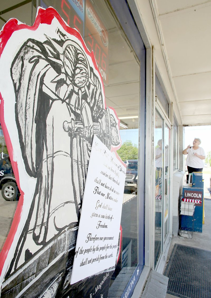 DAVID GOTTSCHALK NWA DEMOCRAT-GAZETTE The patriotic-themed mural, "We Mourn," is visible as Cheryle Prince-Porter continues to paint last week on the window of the Quick-a-Way convenience store in Lincoln. Prince-Porter is painting six patriotic-themed murals on store front windows for the upcoming Memorial Day holiday.