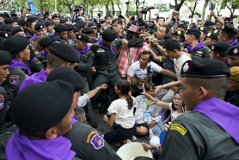 Thai police in Bangkok on Tuesday scuffle surround pro-democracy leader Nuttaa Mahattana (seated with her hands raised) during a protest marking the fourth anniversary of the military takeover of the government.  
