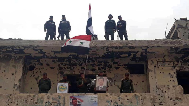 In this photo released by the Syrian official news agency SANA, Syrian military and police forces fly their national flags on a damaged building and hold a picture of Syrian President Bashar Assad, in the Hajar al-Aswad neighborhood, southern Damascus, Syria, Tuesday, May 22, 2018. Syrian state TV said Tuesday the military and police forces are celebrating recapturing the last neighborhoods in Damascus that were held by the rebels and the Islamic State group. (SANA via AP)