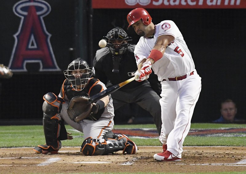 FILE - In this May 2, 2018, file photo, Los Angeles Angels' Albert Pujols, right, hits a solo home run in front of Baltimore Orioles catcher Caleb Joseph, left, and home plate umpire Roberto Ortiz during the first inning of a baseball game in Anaheim, Calif. Baseballs really are getting extra lift, and it's not from the exaggerated upper cuts batters are taking, according to a 10-person committee of researchers hired by the commissioner's office. (AP Photo/Mark J. Terrill, File)