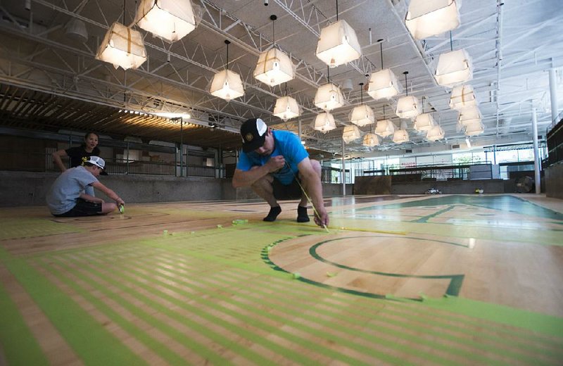 Graham Edwards (right) of Bella Vista prepares to work on the design for a shuffleboard game at a work/play space called The Holler at 8th Street Market in Bentonville while Yume Rudzinski of Fayetteville, the project manager of the space, and Kane Rudzinski (left), 14, work on another section. 
