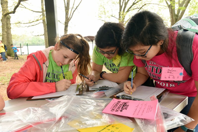 Carley Harris (from left), Mallory Price and Melina Rice write their outdoor stories on May 4 during Lingle Middle School Outdoor School held at Prairie Creek park on Beaver Lake. 