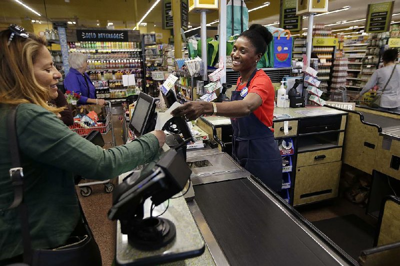 In this May photo, Nadine Vixama, who emigrated from Haiti eight years ago, works as a cashier (right) at a Whole Foods in Cambridge, Mass.  
