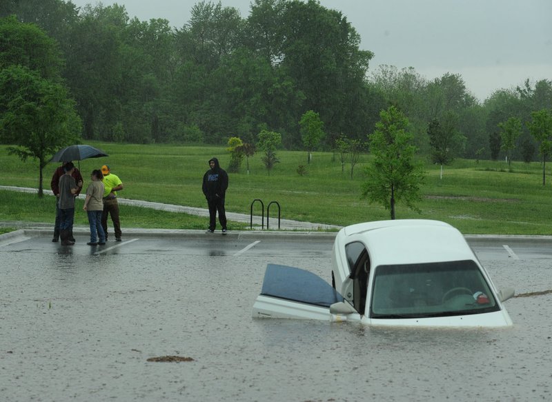 Residents stand near a passenger car in April 2017 after it left the pavement and ended up in a drainage area in the middle of a parking area south of the Botanical Garden of the Ozarks in Fayetteville. The City Council on Tuesday will consider hiring a consultant to closely examine the city's drainage needs.