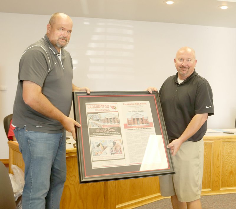 LYNN KUTTER ENTERPRISE-LEADER Farmington School Board President Jeff Oxford, left, presents high school Principal Jon Purifoy with framed pages from a special newspaper section produced by the Enterprise-Leader to celebrate the first 100 days of the new high school building.