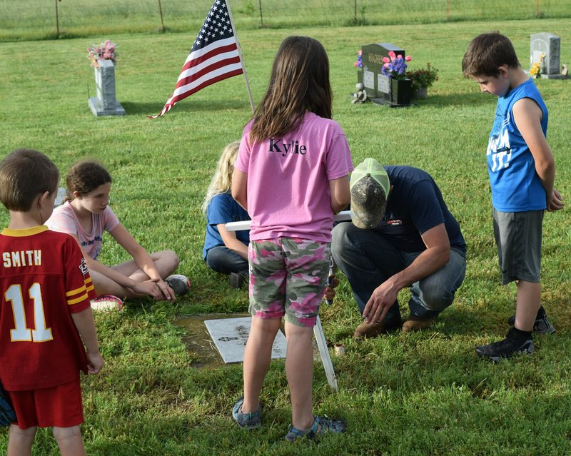Westside Eagle Observer/MIKE ECKELS A group of Decatur 4-H members help Nathan Severs (second from right) plant a metal cross on the grave of a military veteran at the Falling Springs Cemetery in Decatur May 23. The 4-H members placed crosses at the graves of all military veterans to commemorate Memorial Day.
