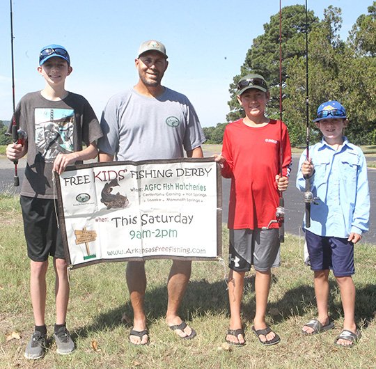 The Sentinel-Record/Richard Rasmussen FISHING DERBY: From left, Carson Armstrong, Jeff Newman, Andrew H. Hulsey State Fish Hatchery manager, Griffin Ralph and Gavin Ralph display a poster promoting Saturday’s annual Kids Fishing Derby at the hatchery. Prizes will be given and drawings will be held throughout the event.