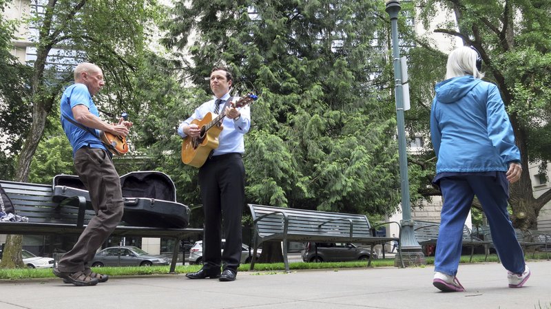 Mack Stilson, left, plays his mandolin and Victor Reuther, right, plays his guitar in a park in Portland, Ore., as they practice for an upcoming bluegrass gig during their lunch hour on June 7, 2018. Stilson and Reuther, both Portland residents, say they are proud of the city's reputation for activism but they are concerned about dueling demonstrations that have turned violent in the past year in downtown Portland. A right-wing group called Patriot Prayer and self-described left-wing anti-fascists clashed in the streets on June 3, in some cases drawing blood, and police made four arrests. (AP Photo/Gillian Flaccus)