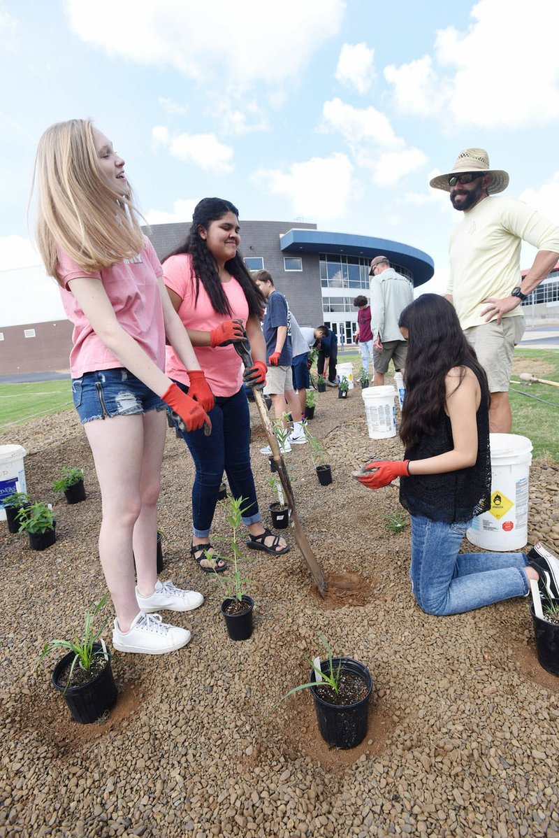 NWA Democrat-Gazette/FLIP PUTTHOFF 
MEMORIAL RAIN GARDEN
Vada Ledbetter (from left), Karina Rascon and Elisa Vasquez, all students at Heritage High School in Rogers, plant a rain garden Tuesday May 22 2018 at the high school with help from Kip Kruger (right), a Heritage teacher and football coach. Environmental science students planted native plants in the garden that is designed to decrease rain runoff from a school parking lot and lessen pollutants coming from the asphalt. A green infrastructure grant from the Illinois River Watershed Partnership funded the garden, said Stephaniw Burchfield with the partnership. The rain garden is a memorial to the late Linda Allen, a Heritage teacher, said Teresa Sidwll, Allen's sister.