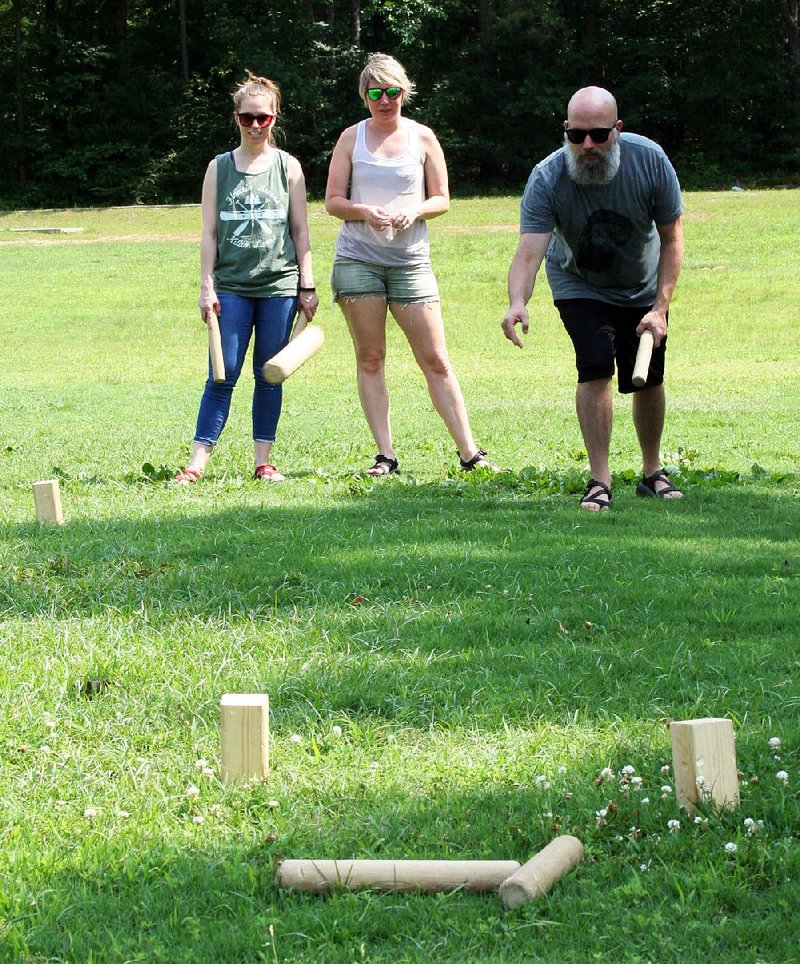 Sasha O’Quin (from left) and Ramona Hicks watch as Kyle Hicks tosses a baton at wooden blocks called kubbs during a game of Kubb at Burns Park in North Little Rock.  