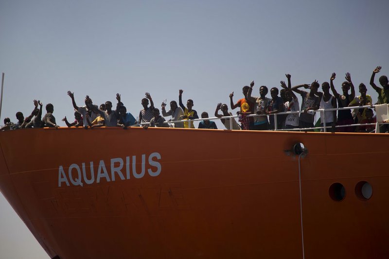 In this photo taken on Sunday, Aug. 21, 2016, migrants wave from SOS Mediterranee Aquarius rescue ship, after being rescued by members of the Spanish NGO Proactiva Open Arms during an operation at the Mediterranean sea, about 12 miles north of Sabratha, Libya. 