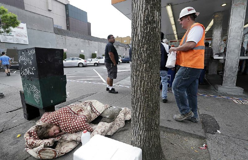 A man sleeps on the sidewalk as people line up to buy lunch at a Dick's Drive-In in Seattle in May. The Seattle City Council has repealed a month-old tax on large employers that was intended to fund programs for the homeless.  