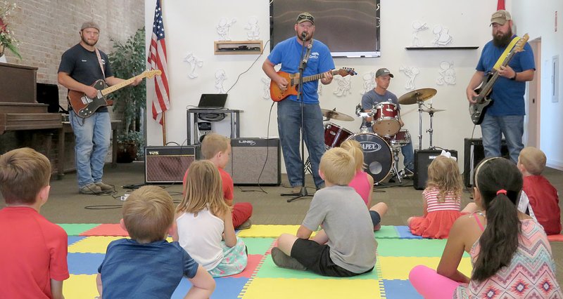Westside Eagle Observer/RANDY MOLL Children were treated to some &quot;rockin' music&quot; at the opening session of the Gentry Public Library's summer reading program on June 5. The musicians, dubbed by Mayor Kevin Johnston as the Public Works Band, are Chase Shawver (left), Mark Bunce, Jeremy McJunkin and Clint Osborne (on the drums). The band members work for the city of Gentry, in the public works department by day but play music together after hours. They were called in to help kickoff the summer reading program because of its focus on music. The June 5 session focused on types of music, and the band members played a variety of music for their young fans.