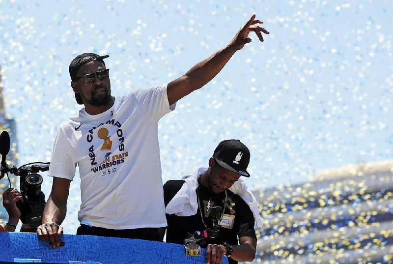 Golden State Warriors’ Kevin Durant (left), who expects a swift re-signing with the team, waves to fans during the team’s championship parade Tuesday in Oakland, Calif.  