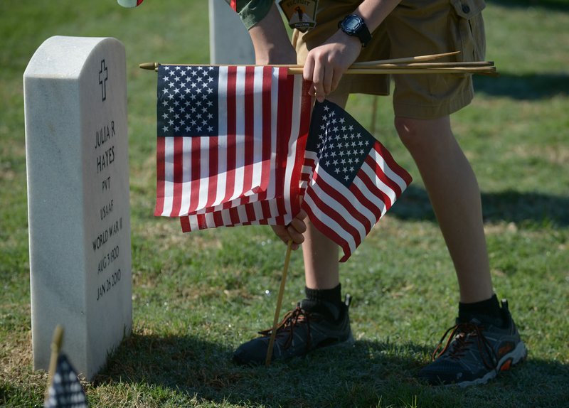 File Photo/NWA Democrat-Gazette/ANDY SHUPE A Boy Scout volunteer places flags May 26 in front of a grave marker at Fayetteville National Cemetery for Memorial Day. 