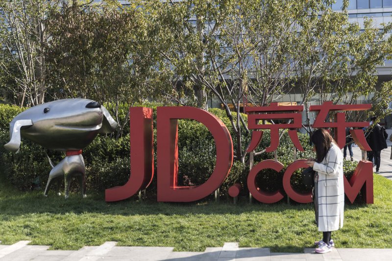 A woman stands next to signage incorporating the logo of JD.com Inc. and the company's mascot &quot;Joy&quot; at the company's headquarters in Beijing on Oct. 23, 2017. MUST CREDIT: Bloomberg photo by Qilai Shen.