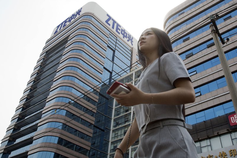 FILE - In this May 8, 2018, file photo, a woman passes by a ZTE building in Beijing, China. Chinese tech giant ZTE Corp.'s chairman promised no further compliance violations and apologized to customers in a letter Friday, June 8, 2018, for disruptions caused by its violation of U.S. export controls, a newspaper reported. (AP Photo/Ng Han Guan, File)