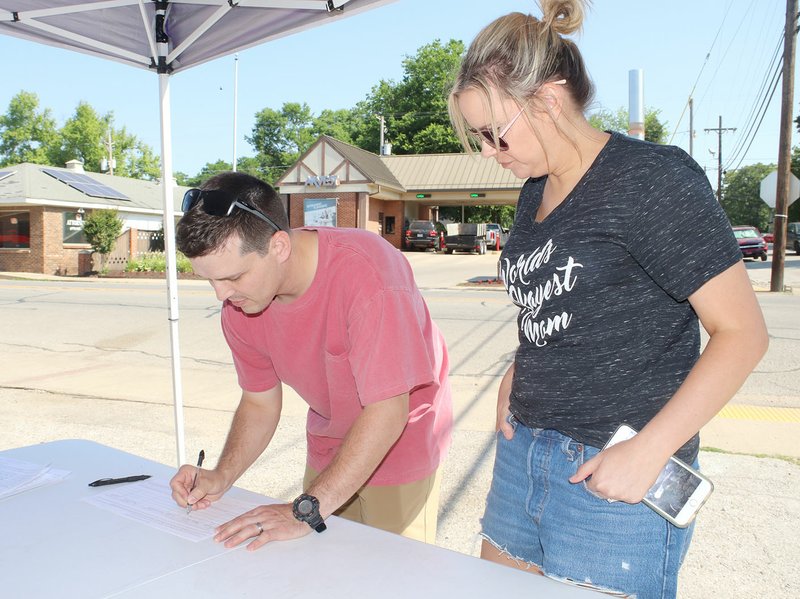 LYNN KUTTER ENTERPRISE-LEADER David and Ashley Taylor of Prairie Grove sign a petition to place a local option question on the ballot to allow the sale of alcohol within all of Prairie Grove city limits. The downtown area in Prairie Grove is dry, based on an election in the 1950s. The committee that initiated the petition drive has suspended its campaign because of time constraints.