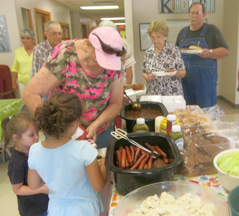 Westside Eagle Observer/SUSAN HOLLAND Kay Cannon helps prepare plates for granddaughters Ella Wright and Holly Cannon at the Senior Activity Center's Father's Day cookout Friday. LaVonda Augustine, Leon Forrest, Juanita Whiteside and Jeff Mortensen wait for their lunch in the background.