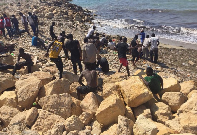 In this Wednesday, June 20, 2018 photo, released by the Libyan coast guard, African migrants who were found on a damaged rubber boat in the Mediterranean Sea and rescued by the Libyan coast guard rest on the shore, east of the capital, Tripoli, Libya. The coast guard said it rescued some 82 African migrants, including four women and two children, and recovered one body. (Libyan Coast Guard via AP)