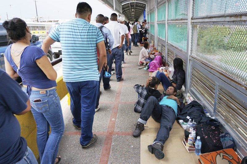 In this Thursday, June 23, 2018 photo, migrant families rest from their travels to Matamoros, Mexico, along Gateway International Bridge which connects to Brownsville, Texas, as they seek asylum in the United States. (Miguel Roberts/The Brownsville Herald via AP)