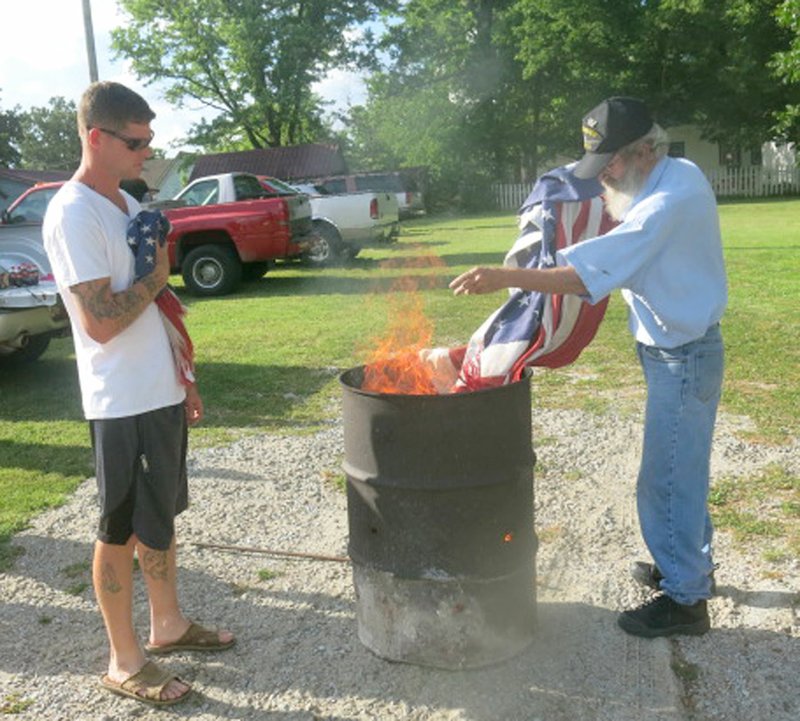 Westside Eagle Observer/SUSAN HOLLAND Nick Croasdell, member of John E. Tracy American Legion post, waits while Will Crose, past first vice-commander for the post, oversees the burning of a retired American flag. Members of the Gravette group hold a flag retirement ceremony each year to retire flags which become faded and worn and are no longer serviceable.