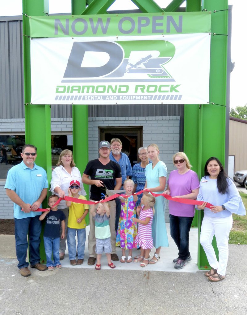 Westside Eagle Observer/RANDY MOLL Tyler and Janae Burns, with their children, family members and guests, cut the ribbon to their new business, Diamond Rock Rental and Equipment, on Arkansas Highway 59 in Gentry, Friday, June 22, 2018. Among those accompanying the Burns Family were Janae's parents, Max and Rose Koehn; Kevin Johnston, Gentry's mayor; Janie Parks, executive director of the Gentry Chamber of Commerce; Tammie Runyan, president of the Gentry Chamber of Commerce; and Andrea Tun, manager of the Gentry branch of Grand Savings Bank.