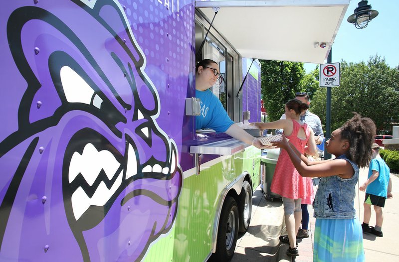 NWA Democrat-Gazette/DAVID GOTTSCHALK Kassidy Meadows, 8, receives a chicken sandwich with glazed carrots Monday, June 4, 2018, from Sheri Clayton, manager of the Fayetteville Public Schools Child Nutrition Mobile Food Trailer, in front of the Fayetteville Public Library. The library is the new additional mobile site for the FPS Summer Lunch &amp; Snack program. The food trailer will be at the library serving lunch from 12:30 pm to 1:00pm Monday through Friday through August 8.
