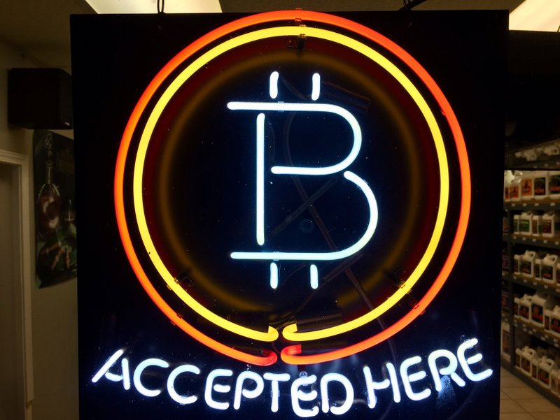 In this Feb. 7, 2018 file photo, a neon sign hanging in the window of Healthy Harvest Indoor Gardening in Hillsboro, Ore., shows that the business accepts bitcoin as payment. (AP Photo/Gillian Flaccus, File)