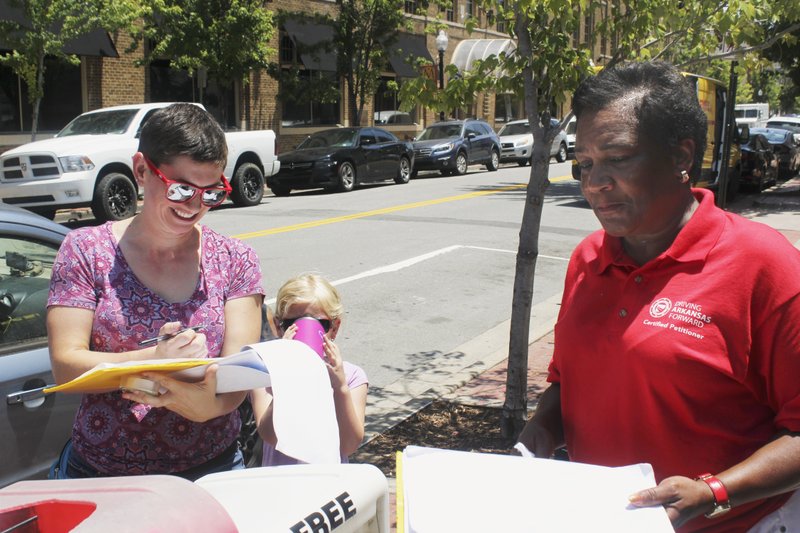 In this Thursday, June 28, 2018, photo, Rachelle Tracy signs a petition in downtown Little Rock, Ark., from canvasser Cynthia Ford in favor of putting a minimum wage hike proposal on the November ballot. Friday, July 6 is the deadline for initiative campaigns to submit signatures to qualify for the ballot. Ford also circulated petitions for the wage hike proposal, along with proposals to impose strict term limits and to legalize casinos. (AP Photo/Andrew DeMillo)

