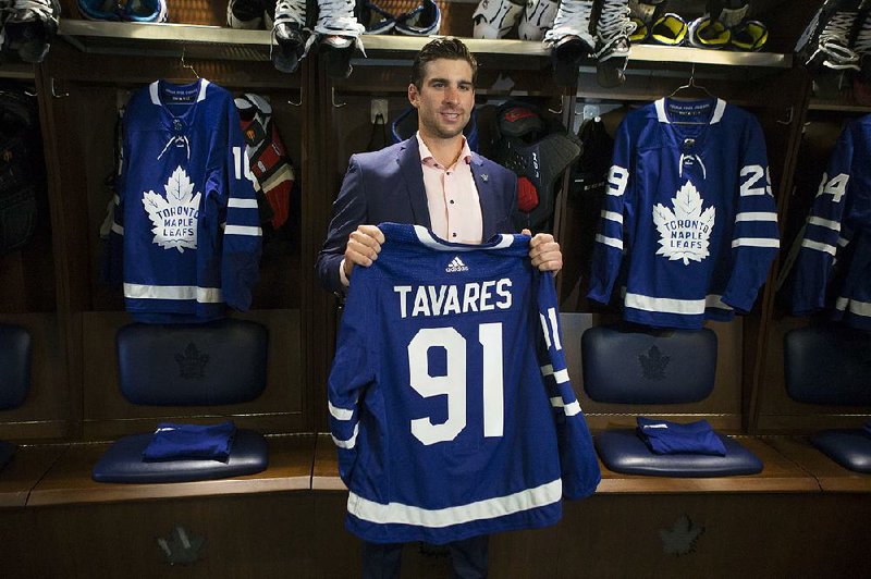 John Tavares holds up a Toronto Maple Leafs jersey in the team’s locker room Sunday after agreeing on a $77 million, seven-year contract. Tavares’ decision to leave the New York Islanders for the Maple Leafs has made the Leafs a strong contender for the Stanley Cup. 