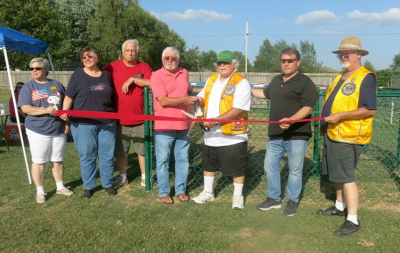 Westside Eagle Observer/SUSAN HOLLAND Danny White (center) joins Gravette Lions Club president Bill Mattler in cutting the ribbon for the new human foosball court at Pop Allum Park. White, owner of Cardinal Pawn in Gravette, contributed materials for the court and Lions Club members did the labor. White and Mattler are joined by Lions Club members Sue Rice, Karen Benson, Howard Benson, Mayor Kurt Maddox and Al Blair.