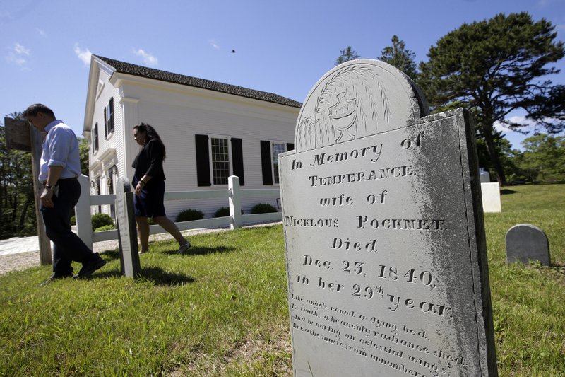 In this Monday, June 25, 2018 photo a gravestone dated 1840, foreground, stands near the Mashpee Old Indian Meeting House, behind, on Mashpee Wampanoag Tribal land, on Cape Cod, Mass. The tribe says an unfavorable decision from the U.S. Interior Department on its tribal reservation status would effectively shut down certain government operations, including the tribe's new court system and police force. (AP Photo/Steven Senne)