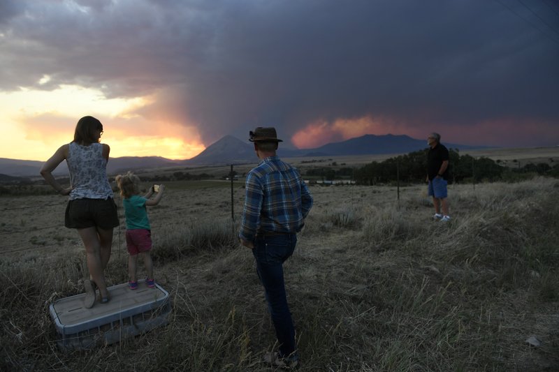 Libby Barbee, left, her daughter Emmy and husband, Brandon Laird, and father, Ron Barbee, right, hold watch as the sun sets over the Spring Fire late Wednesday, July 4, 2018, in La Veta, Colo. They are evacuees who have a family cabin in Cuchara and hoping to go home soon. (Helen H. Richardson/The Denver Post via AP)