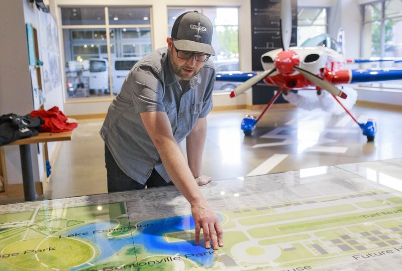 NWA Democrat-Gazette/CHARLIE KAIJO Phillip Johnson, director of OZ1, points at a map Friday of the grounds of the new Flying Club to be built by the end of the summer at the OZ1 Flying Club shop in Bentonville.
