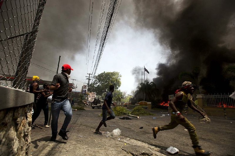 People run from Haitian police officers Saturday as cars burn in the garage of a hotel in Port-au-Prince during a violent protest over planned fuel price increases. The government suspended the increases Saturday after rioters burned tires, looted stores, set fire to cars and attacked at least one hotel.  