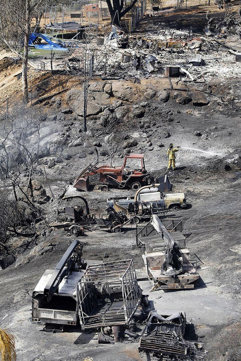 A firefighter puts out hot spots at a home burned by a wildfire in Alpine, Calif., Saturday, July 7, 2018. (Howard Lipin/The San Diego Union-Tribune via AP)